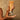 Hand holding a tube of Moroccanoil body scrub with product being poured onto the palm against a brown background.